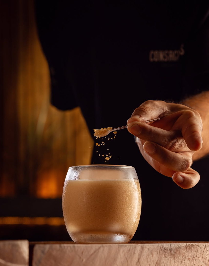 Drink Ouro de Buteco em copo baixo, com o toque final de castanha sendo adicionado com a colher