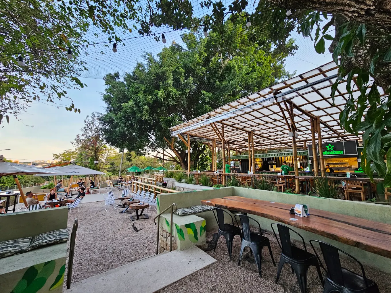 Quintal arborizado de 1200 m² no fim da tarde, com mesas ocupadas e o bar de bambu ao fundo
